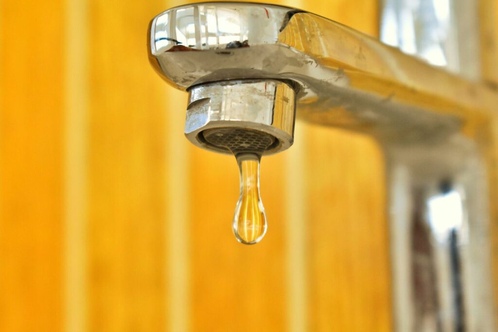 Goutte d’eau suspendue sous un robinet métallique