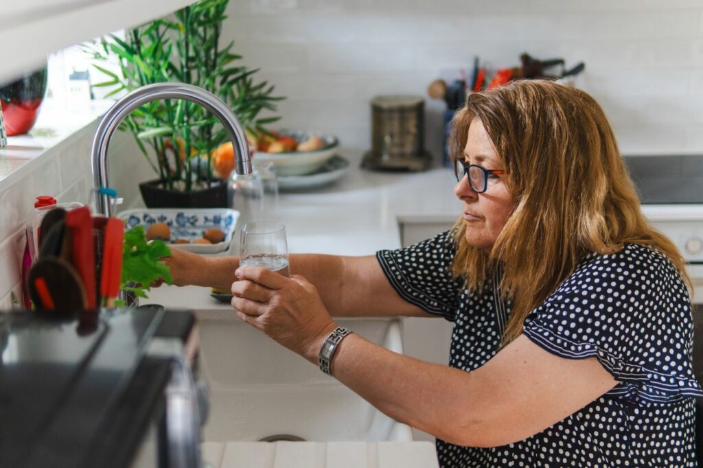 Personne remplissant un verre d’eau dans une cuisine
